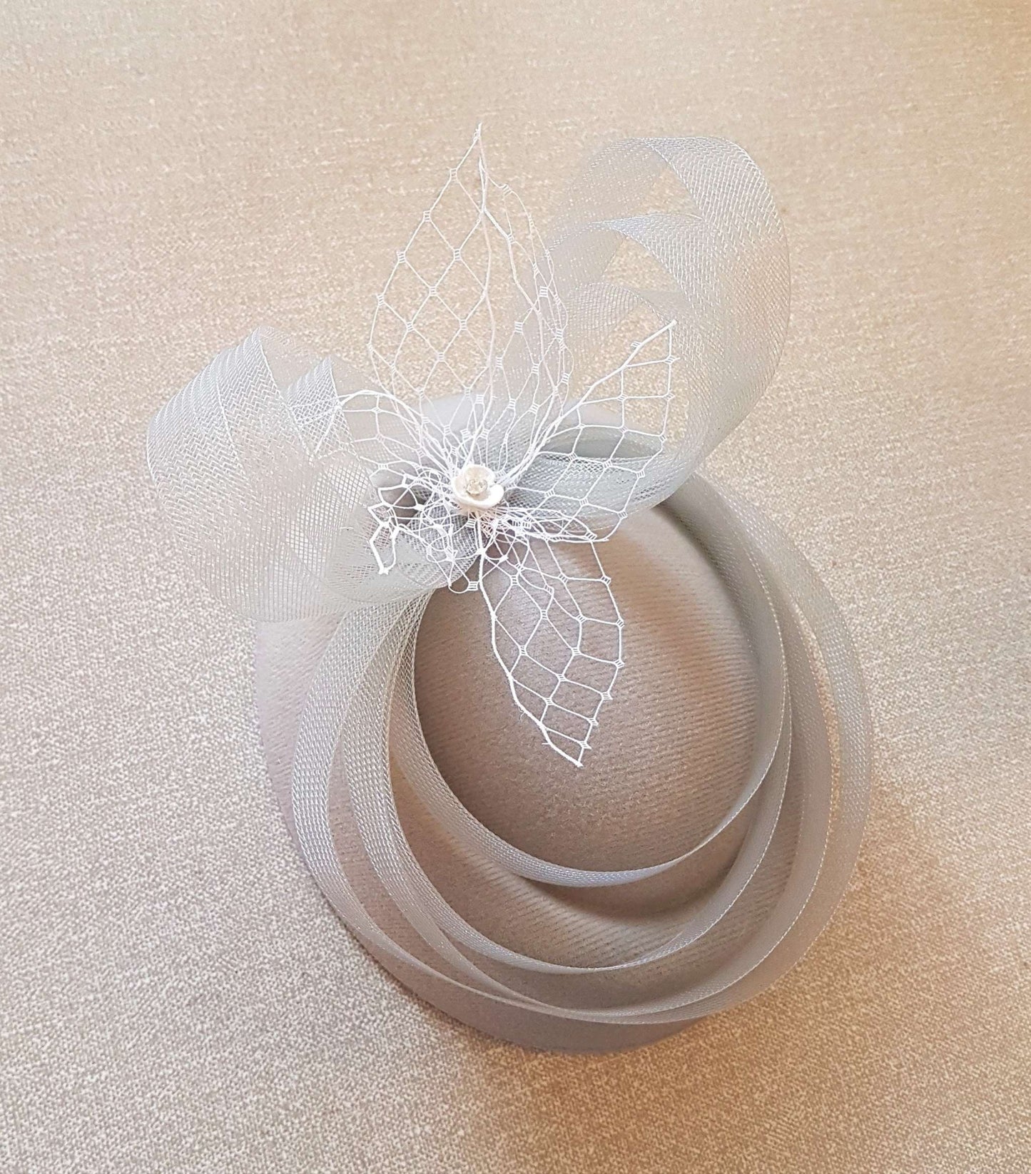 White fascinator hat with crinoline bows, loops, and French net detail; vintage-inspired, ideal for weddings or events.