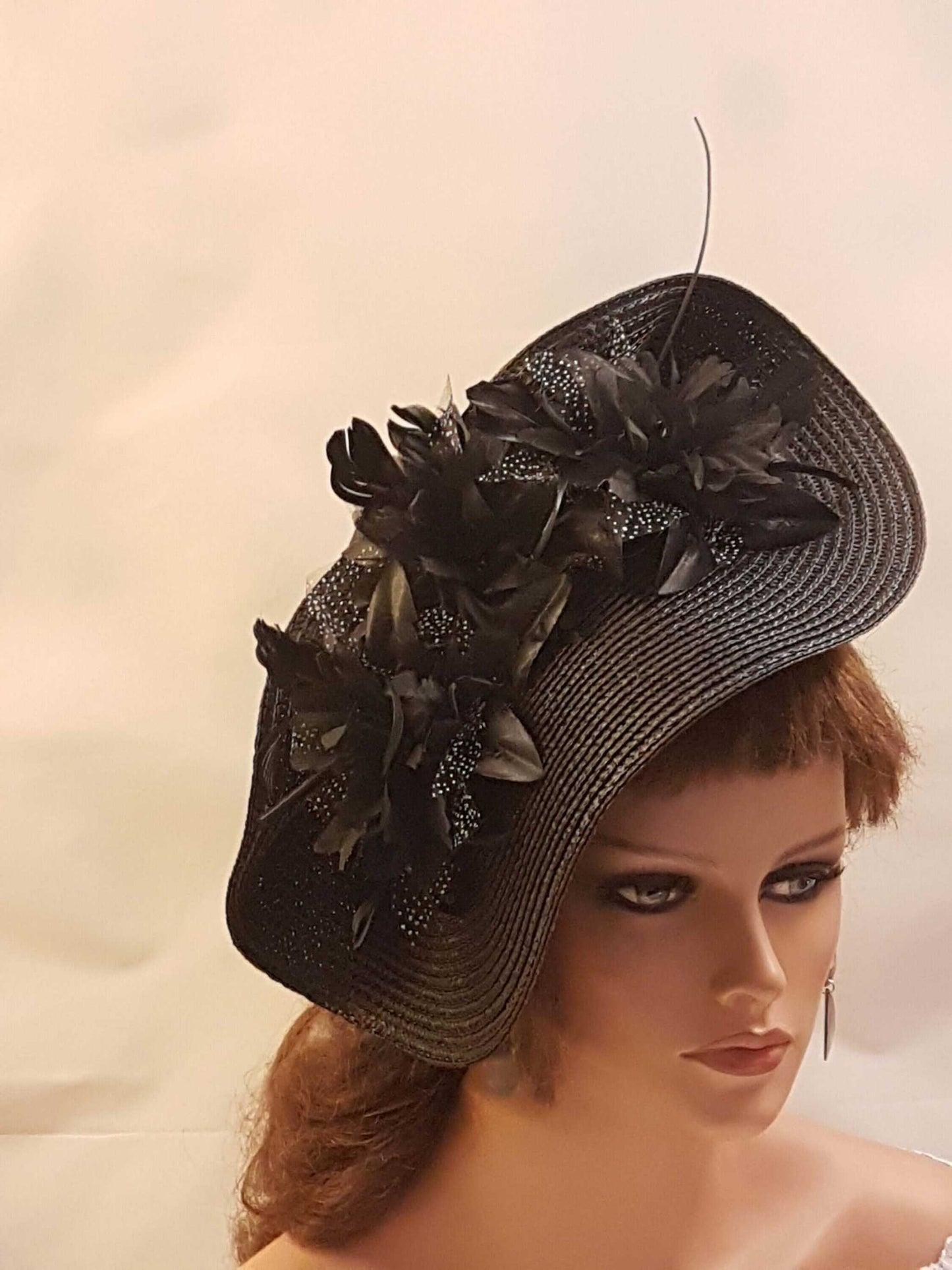 Black hat fascinator with large saucer design, flower and feather accents for weddings and ceremonies.