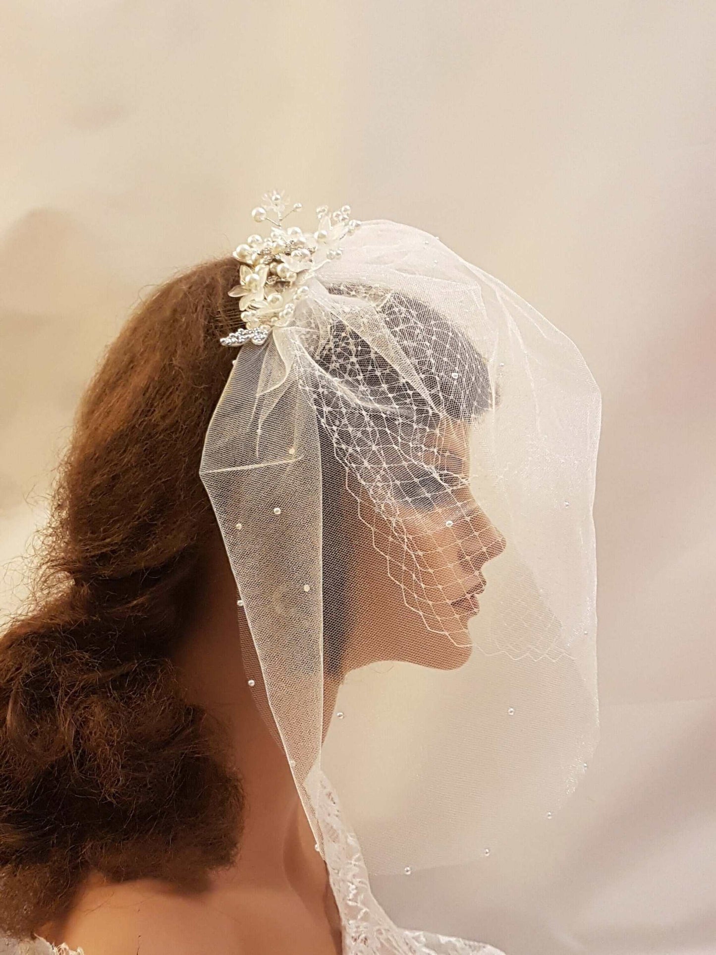 Bridal birdcage veil with lace fascinator and pearls on mannequin.