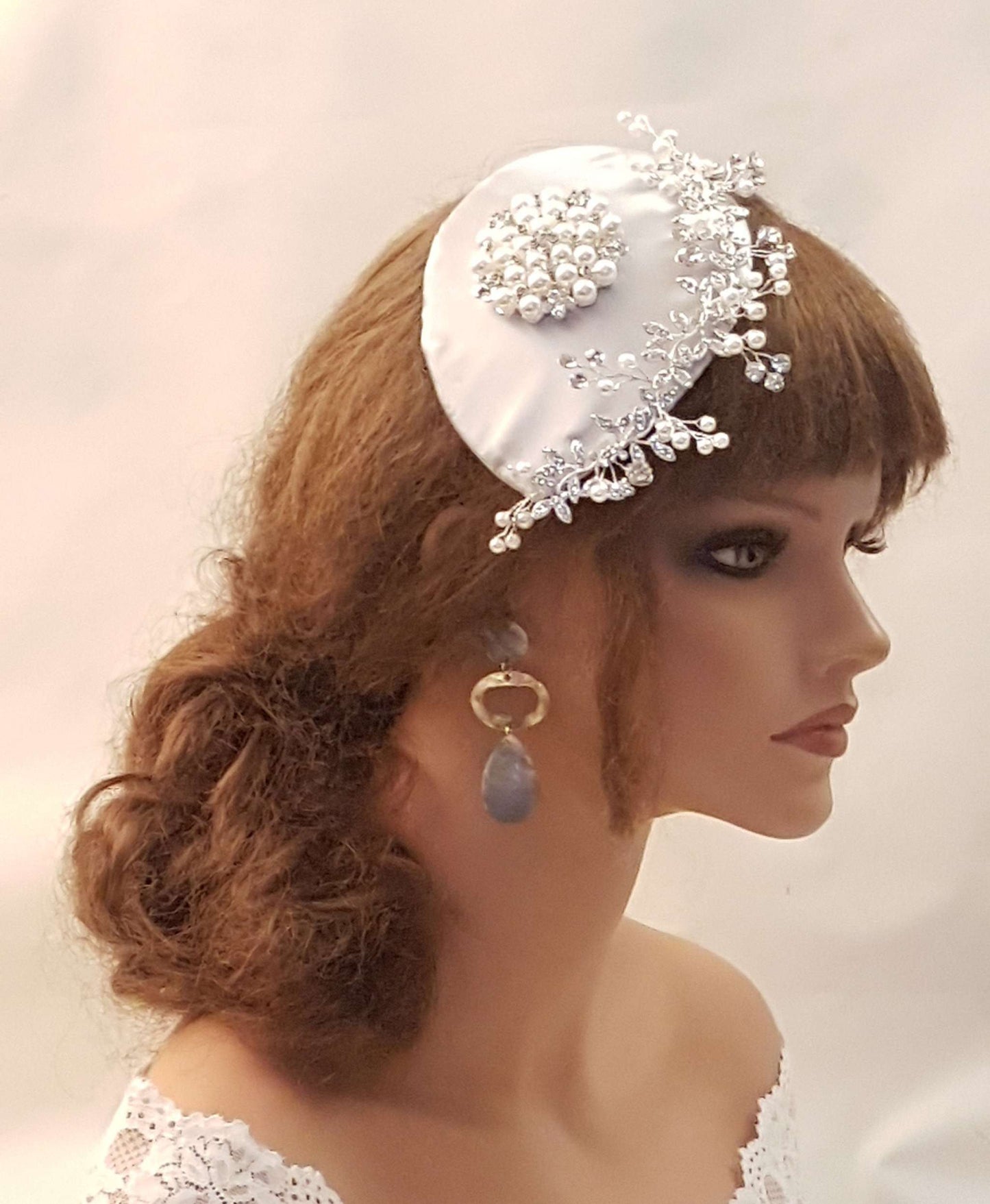 Bridal fascinator with pearl and crystal embellishments, birdcage veil accessory in silver grey, white, ivory, and champagne tones.