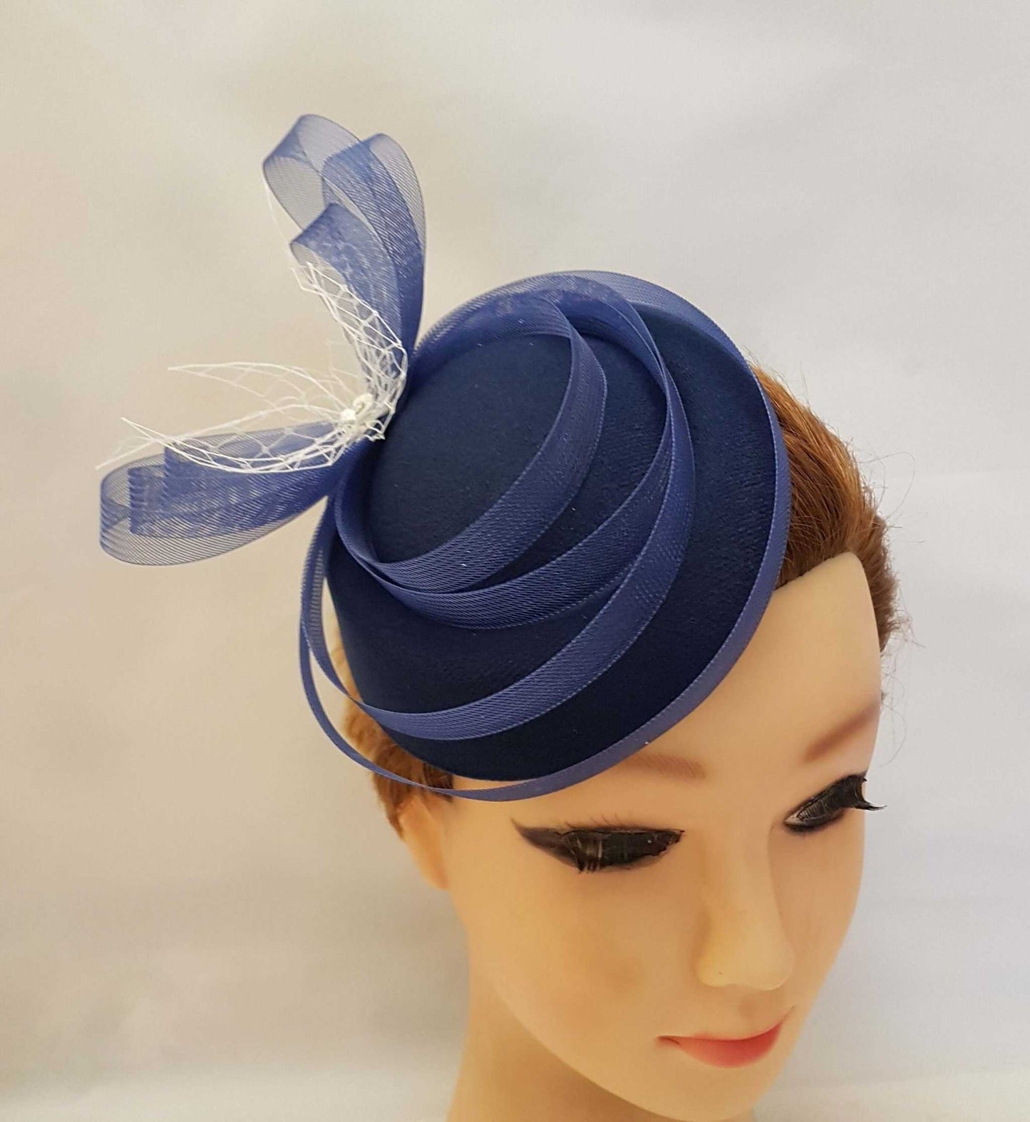 White fascinator hat with birdcage veil and crinoline bows, vintage-inspired bridal headpiece.