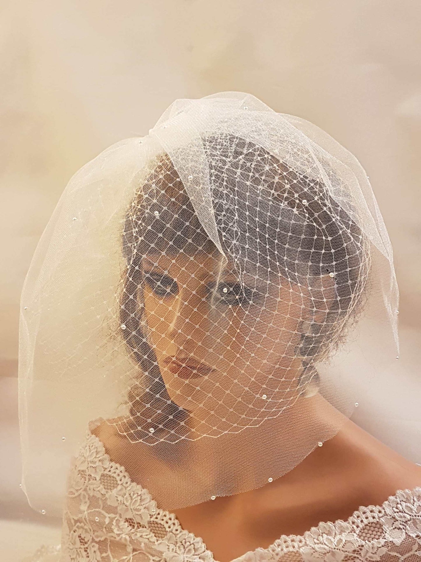 White bridal birdcage veil with lace fascinator, adorned with pearls and crystals for wedding.