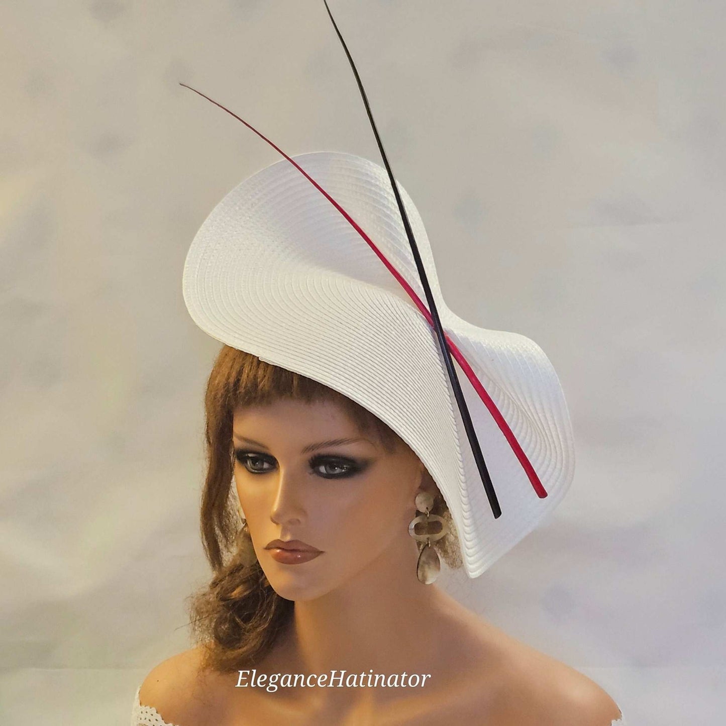 Large white saucer hatinator with red and black quill feathers for weddings and special occasions.