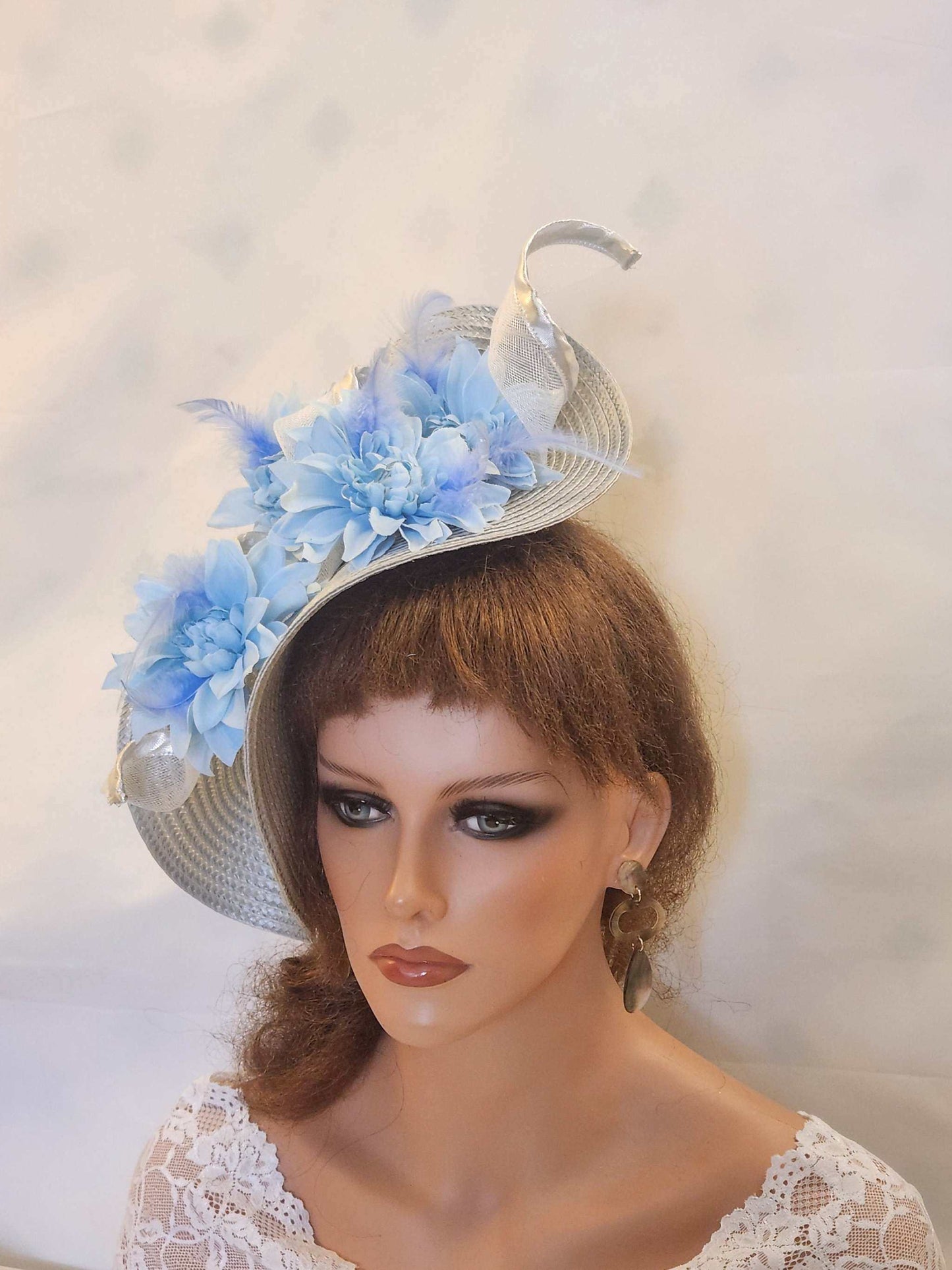 Silver and blue fascinator with floral and feather details, perfect for weddings and races.