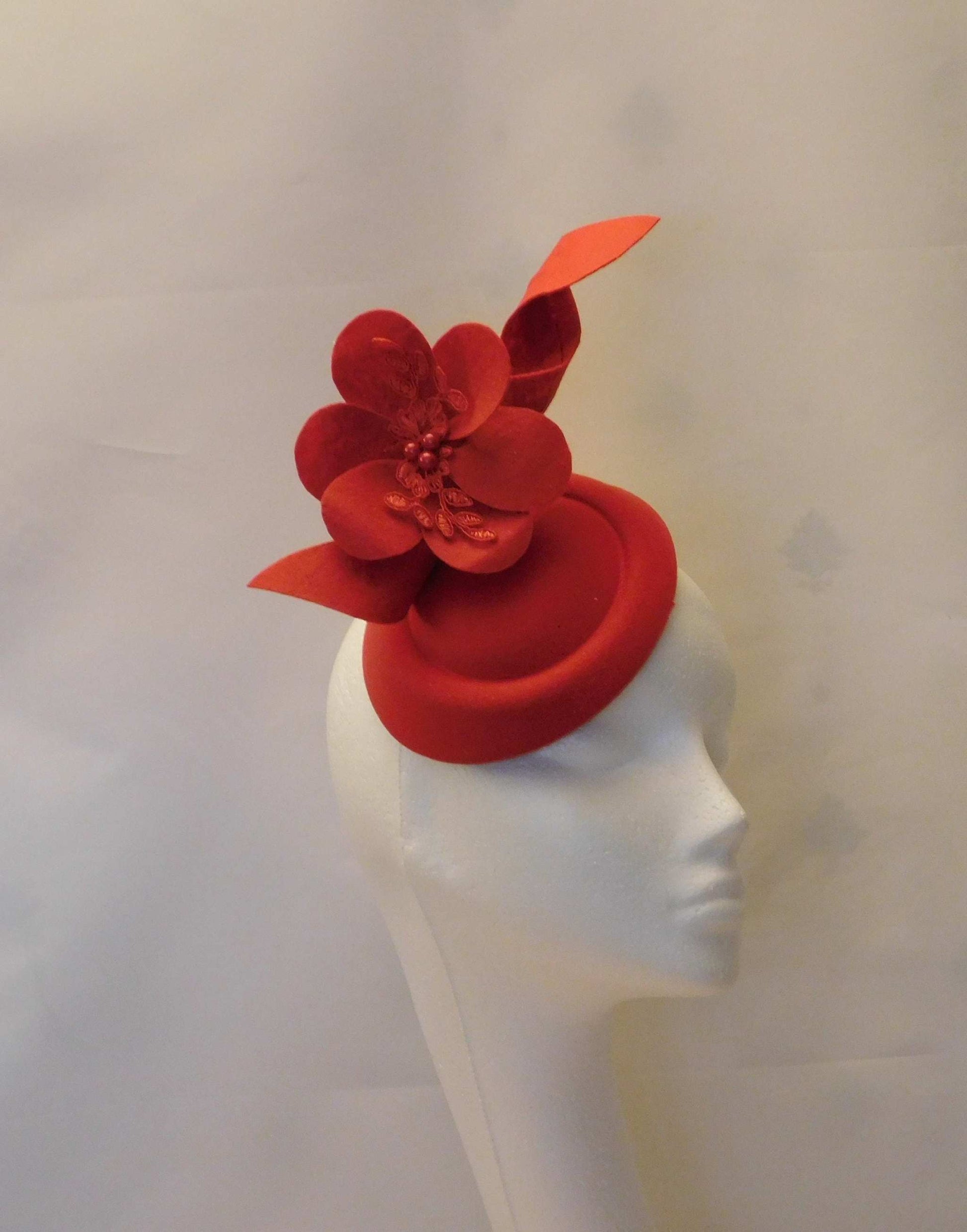 Red fascinator hat with felt flower and swirl design, ideal for weddings, races, and special occasions.