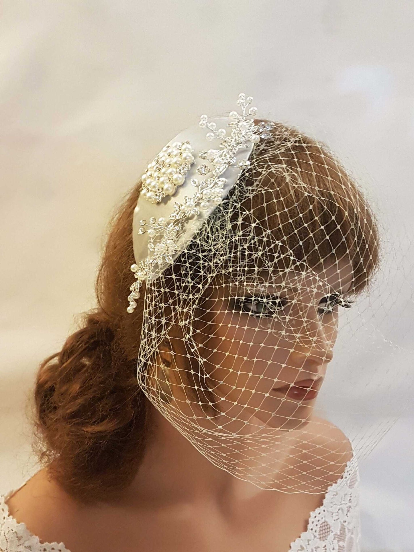 Bridal fascinator with teardrop hat and birdcage veil in silver grey, featuring crystal and pearl embellishments.