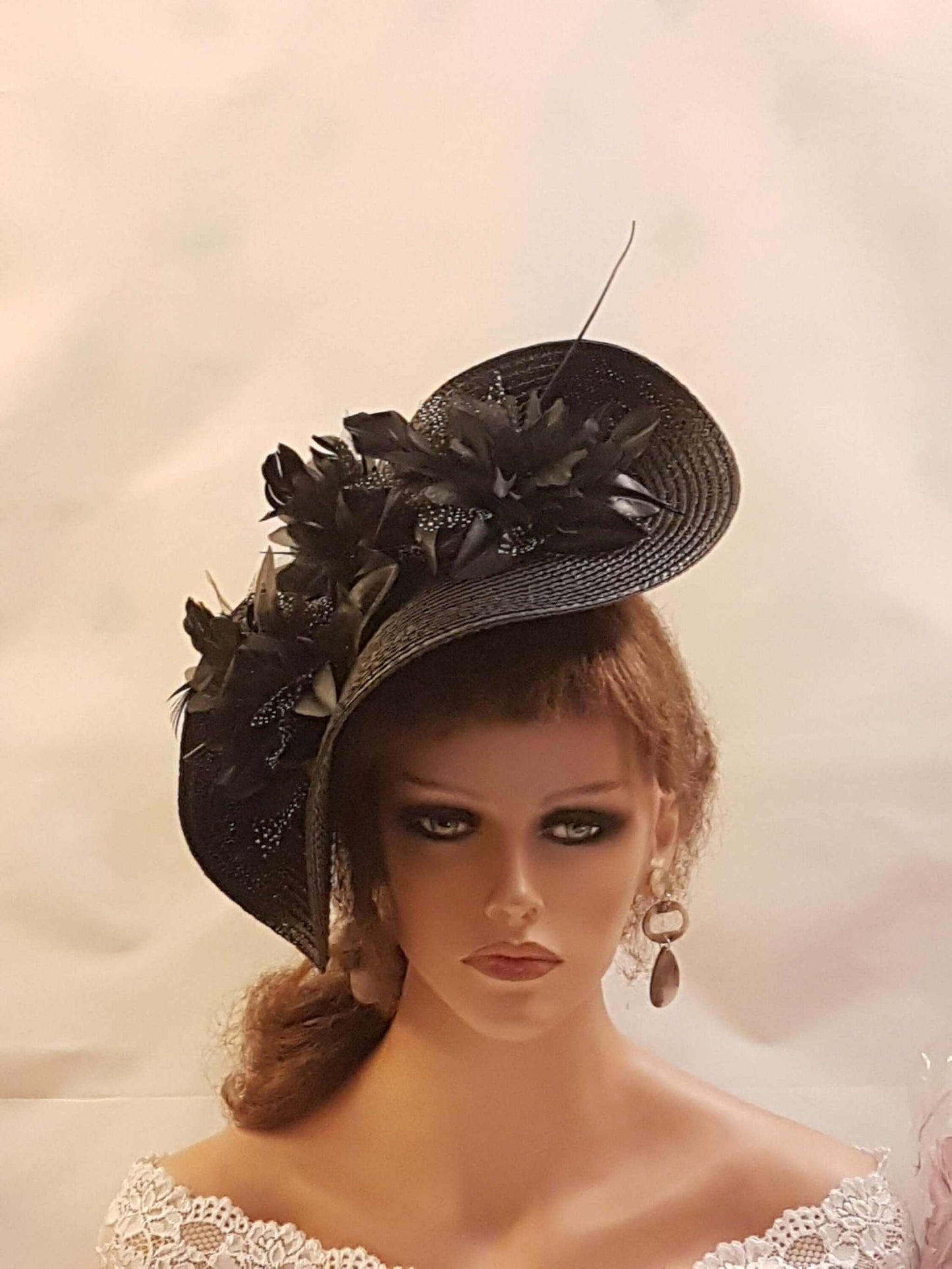 Black hat fascinator with large saucer, flower and feather details, perfect for weddings and ceremonies.