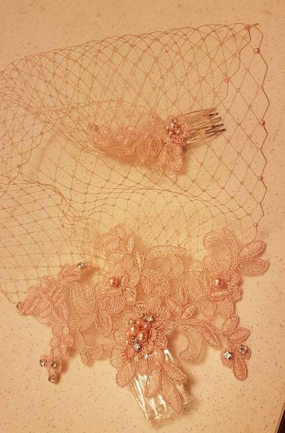 Blush pink birdcage veil wedding accessory with lace, pearls, and crystals attached to silver combs