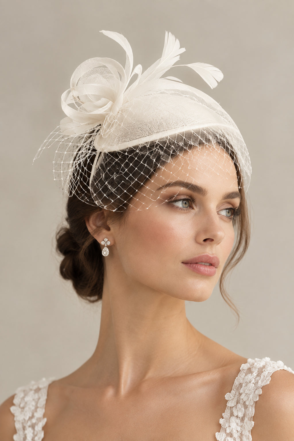 A white or ivory bridal fascinator with a mini birdcage veil attached to a teardrop sinamay hat base, embellished with crinoline roses, leaves, loops, and feathers on a satin-covered headband.