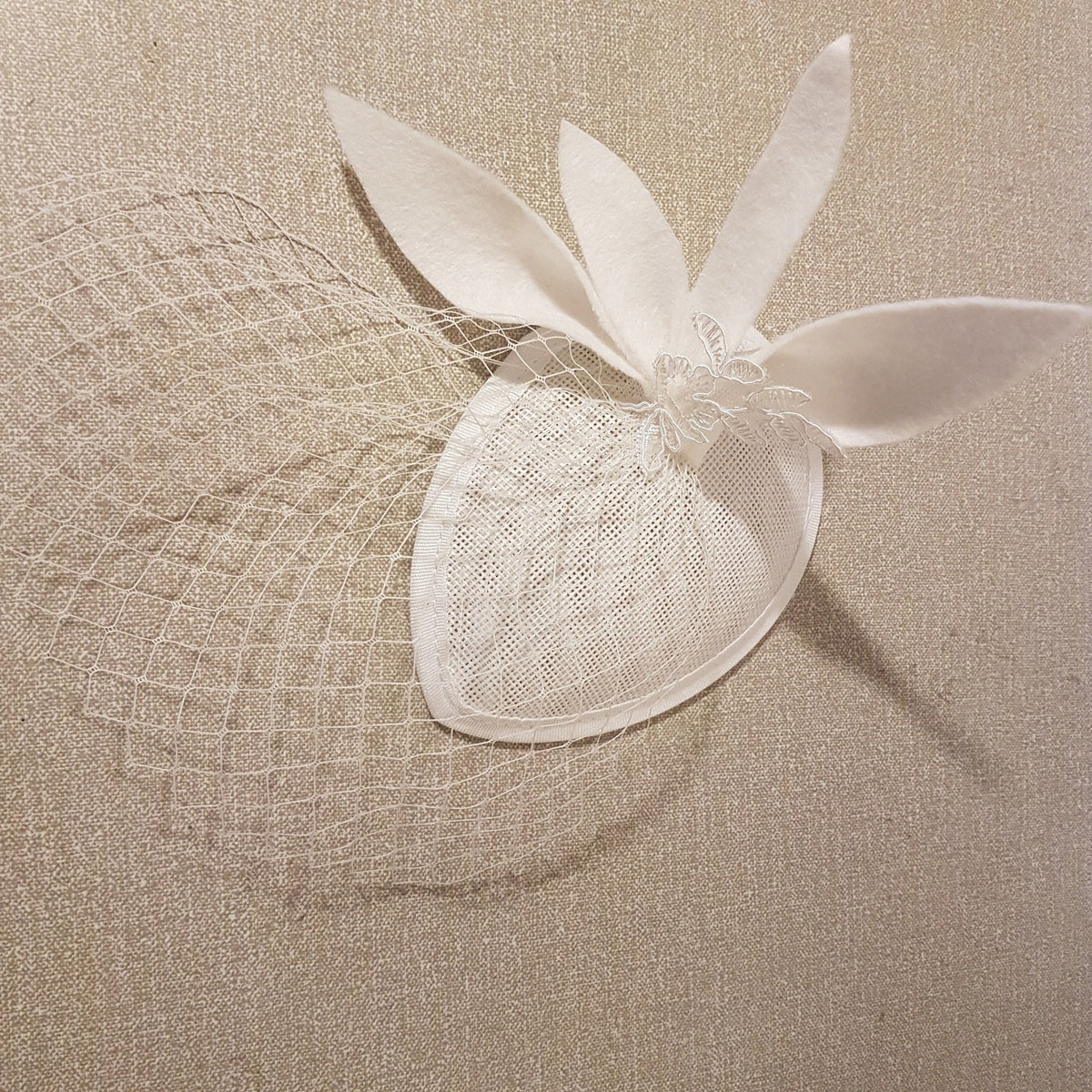 A white bridal fascinator with mini Birdcage veil. The teardrop fascinator base with a delicate lace design and white felt leaves.