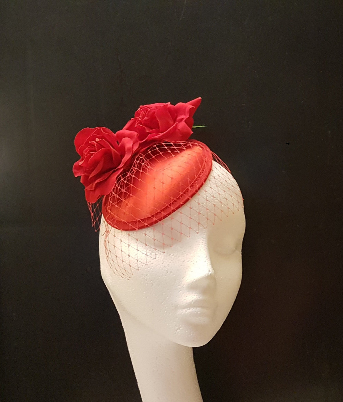 red fascinator hat with a red netting veil and  red fabric roses