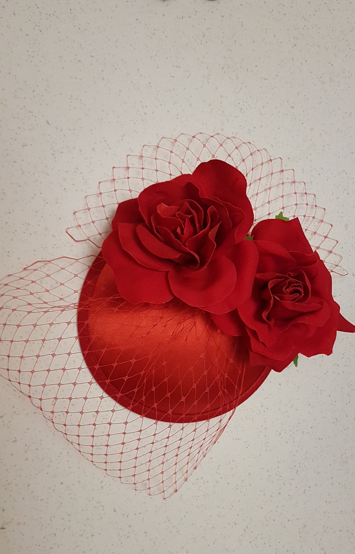 red satin hat with a red netting veil and two red fabric roses