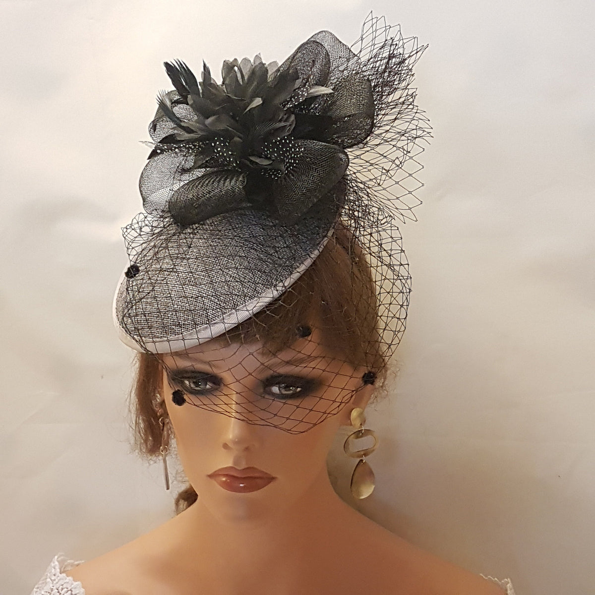 black and Grey fascinator hat with a black net veil. The hat has a white base and a black net overlay with a black flower accent.