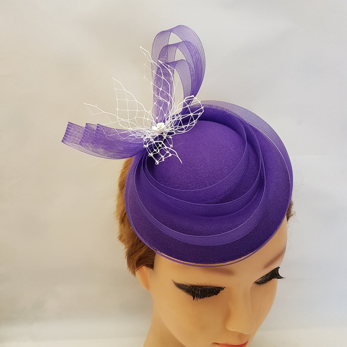 purple felt hats and fascinators. small hat with a white mesh and Crinoline ribbon accent. The hat is a popular choice for weddings and other special occasions.