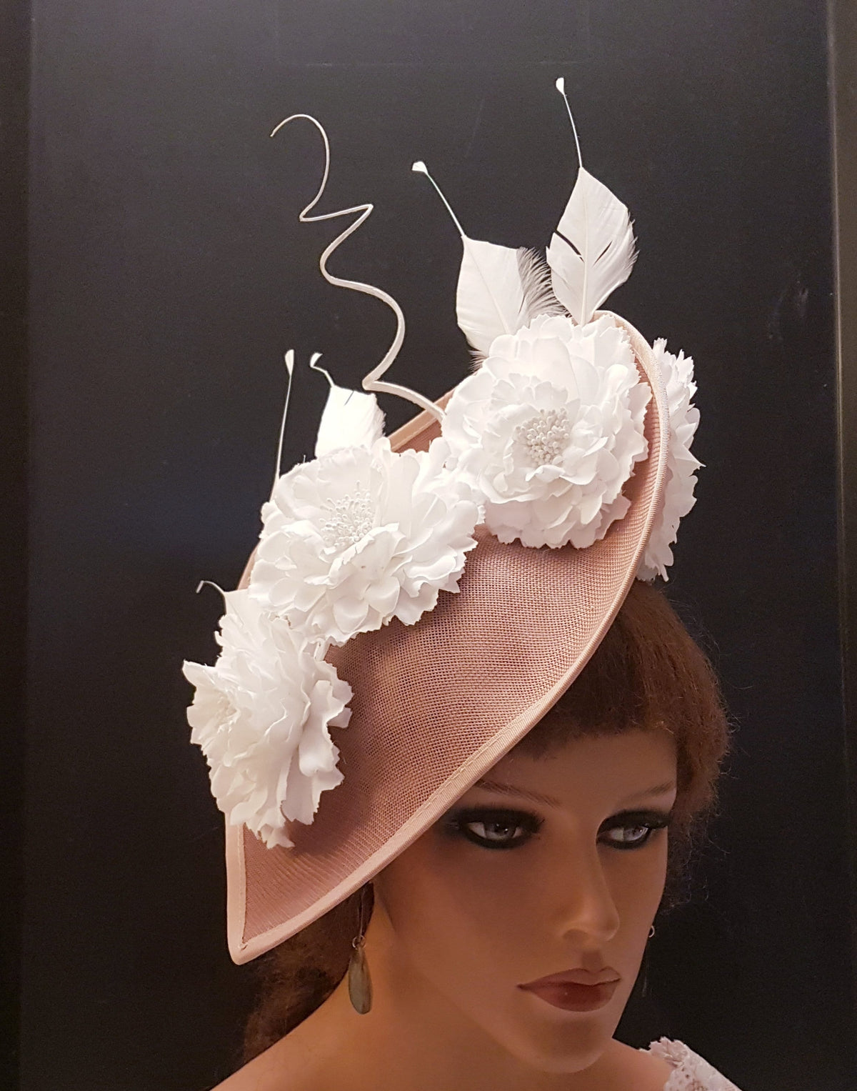 blush pink hat with white fabric flowers and feathers. The hat is angled and has a wide brim.