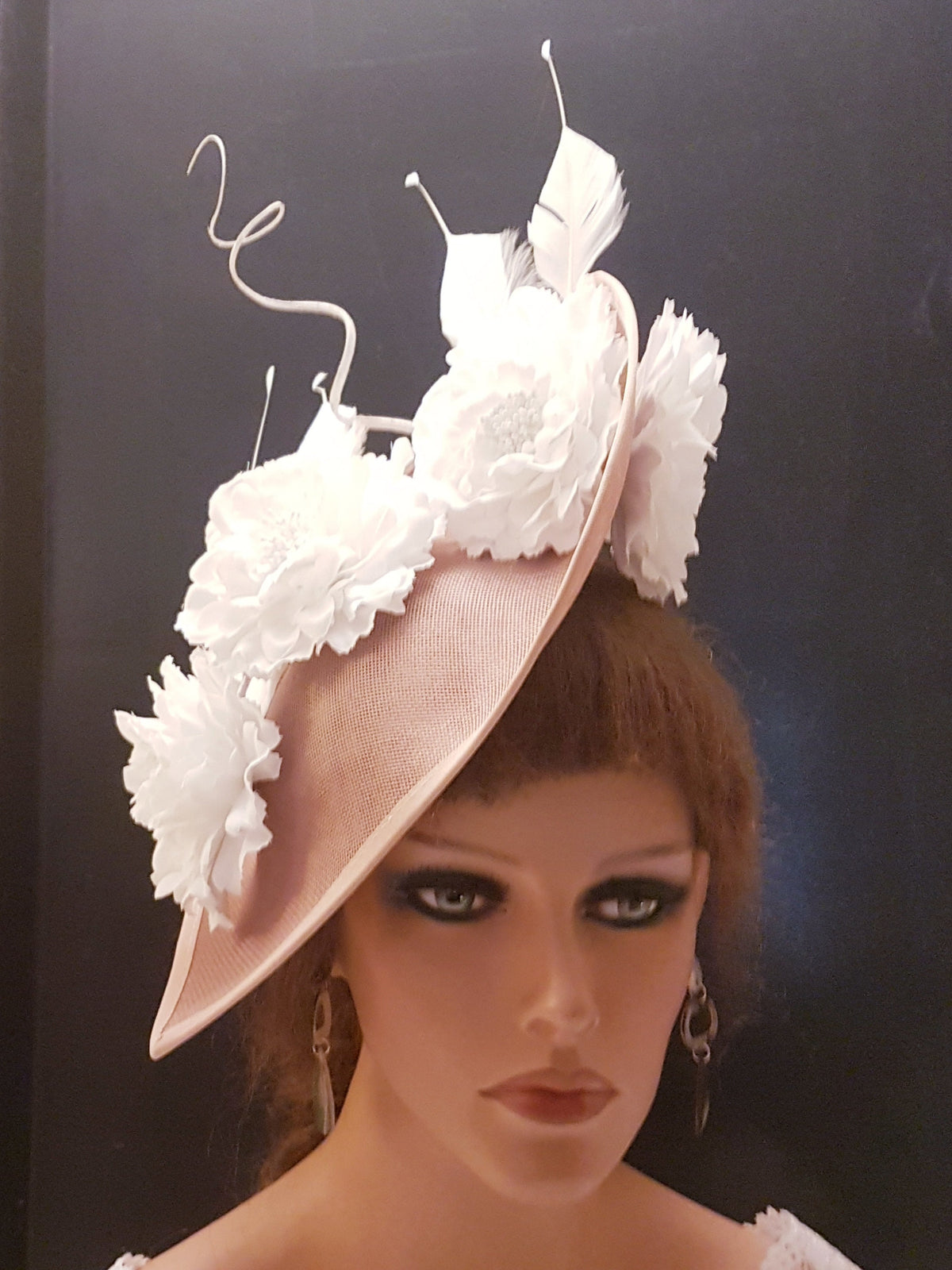 A blush pink fascinator with white flower embellishments and feathers.