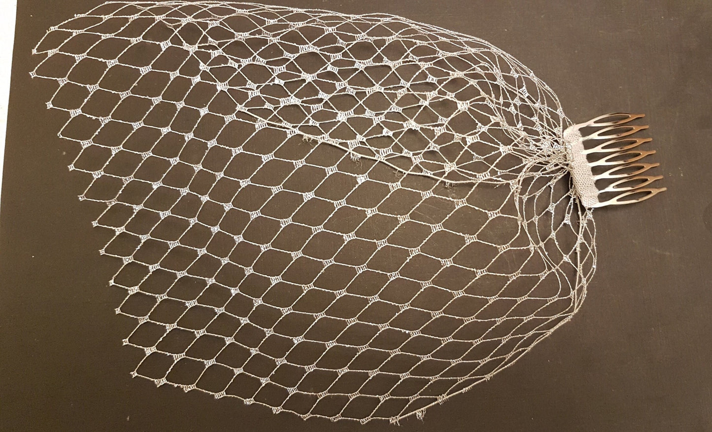 A white bridal veil with a comb attachment. The veil is made of a fine mesh material and has a delicate, lacy pattern.