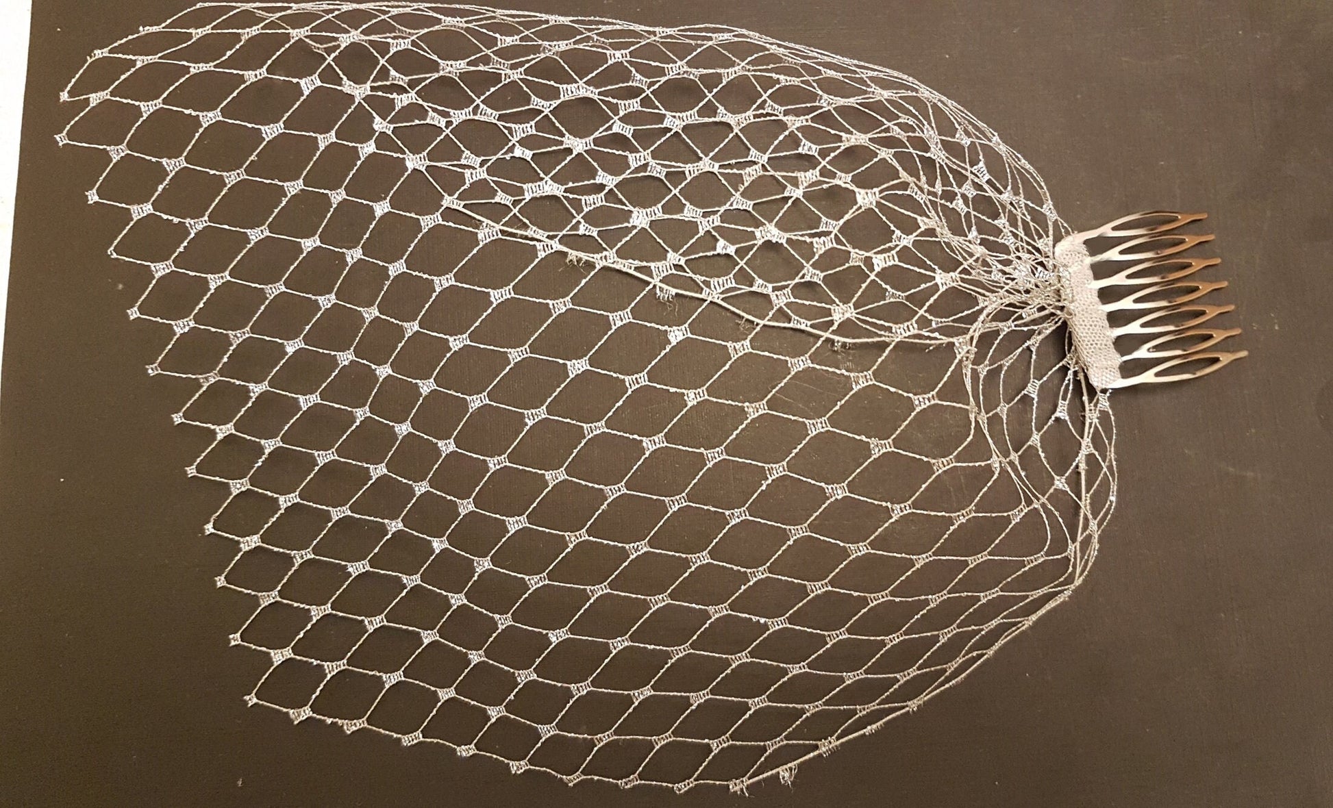 A white bridal veil with a comb attachment. The veil is made of a fine mesh material and has a delicate, lacy pattern.