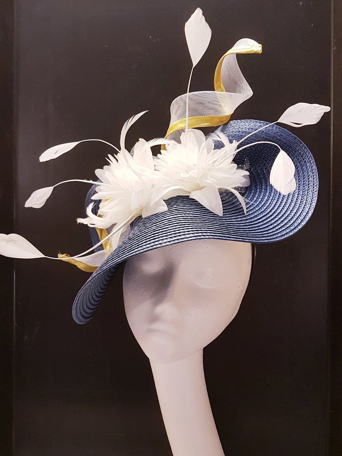 A blue and white Mother of the bride hat with a white flower and feathers.