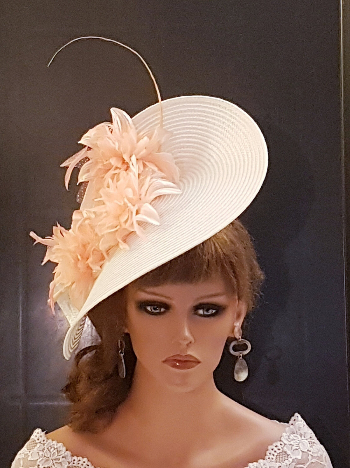 A white wide-brimmed hat with a pink colored flower and feather embellishment.