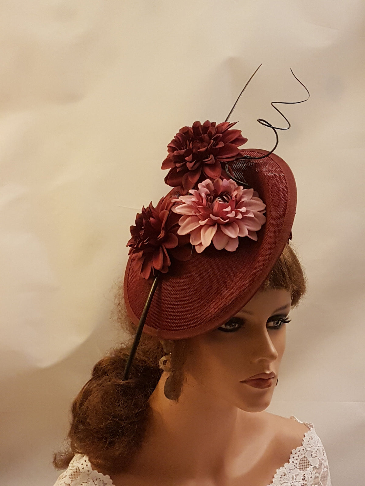 burgundy fascinator with a pink and burgundy flower design. The fascinator has a wire stem that curls at the top.