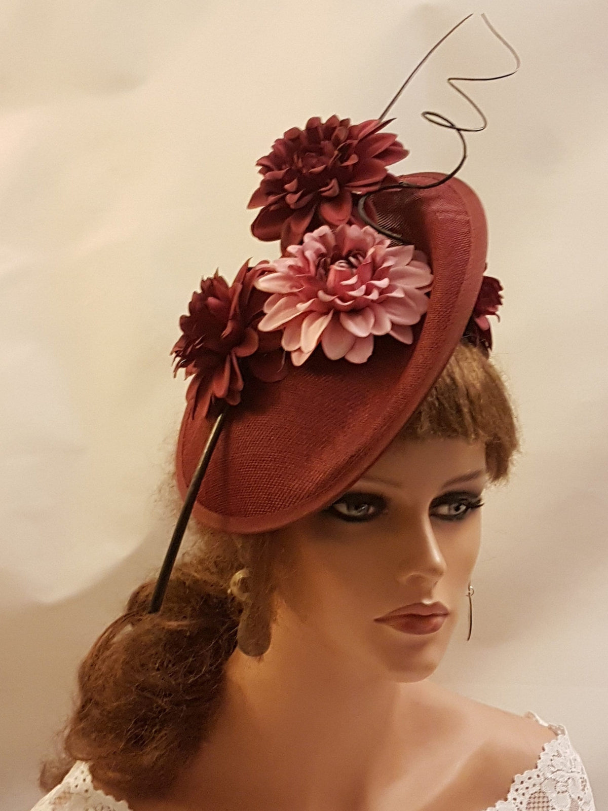 burgundy fascinator with a pink and burgundy flower design. The fascinator has a black wire accent and is perched on a mannequin's head.