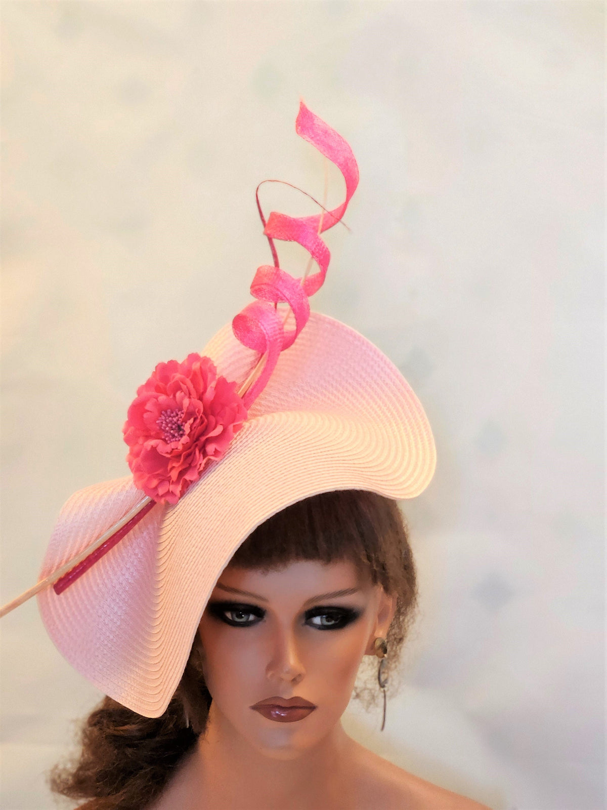 pink hat with a pink flower and a pink ribbon. The hat is made of straw and has a wide brim. The ribbon is curled and is attached to the hat with a pin.