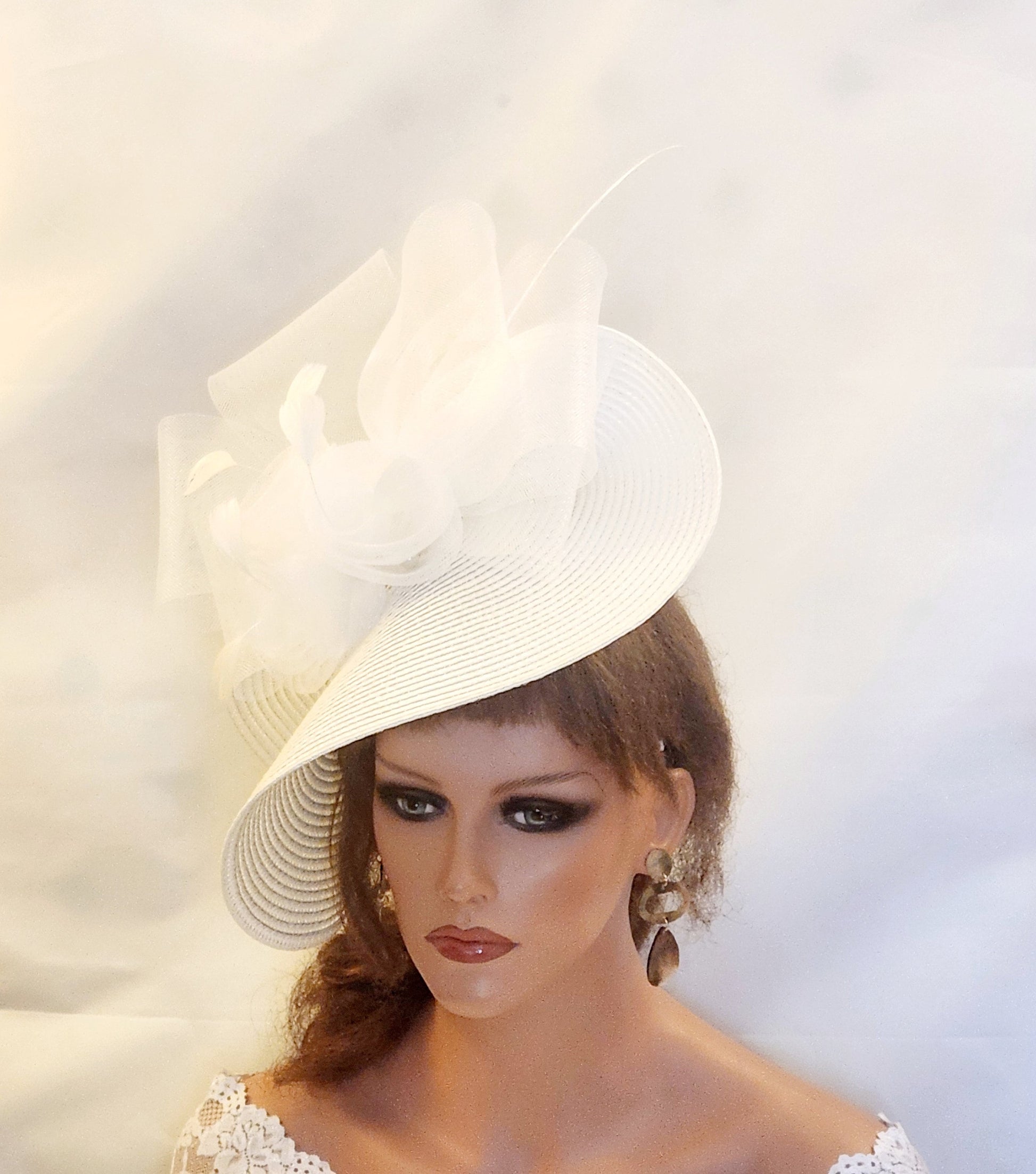 A white wide-brimmed hat with a large white flower on top. The hat is made of pp straw and has a slightly angled brim. The flower is made of a soft, delicate material and has a ruffled appearance.