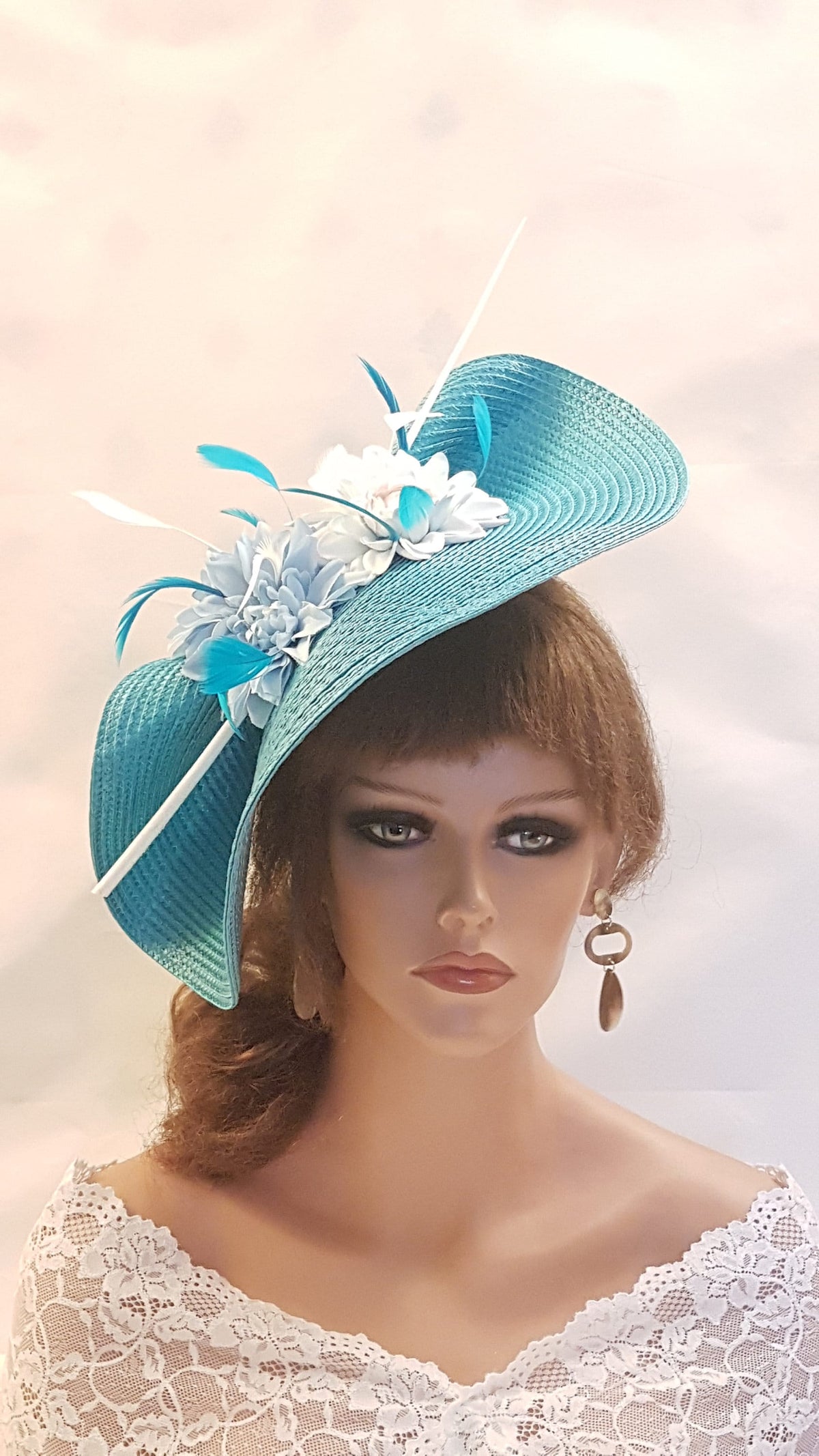 The image displays an elegant teal wide-hat with a decorative arrangement. Straw weave hat is embellished with flowers in white and light blue. feathers in white and teal hues, adding a stylish  accent to the overall appearance of the 
occasion