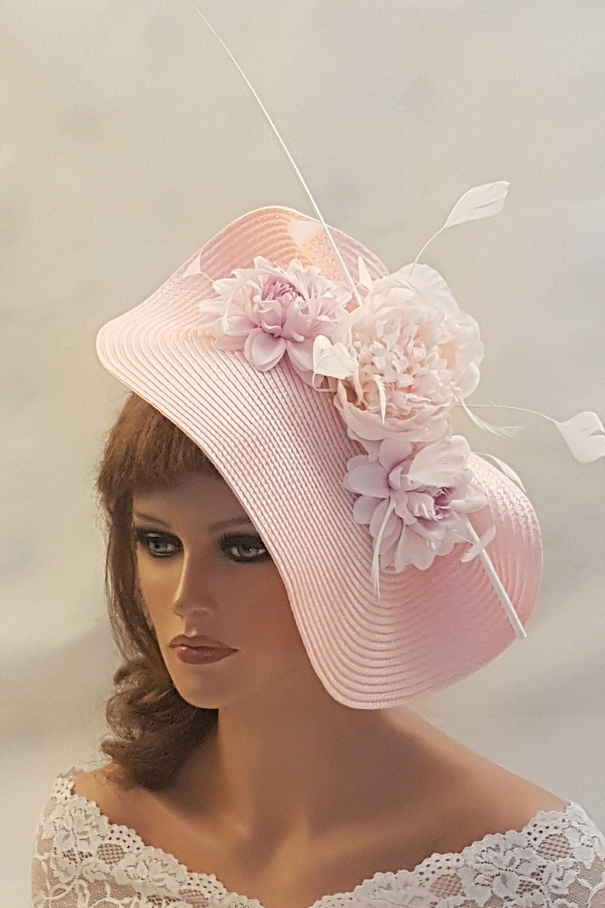 A pink wide-brimmed hat with a large pink flower and two smaller pink flowers on the side. The hat has a white feather on the side.
