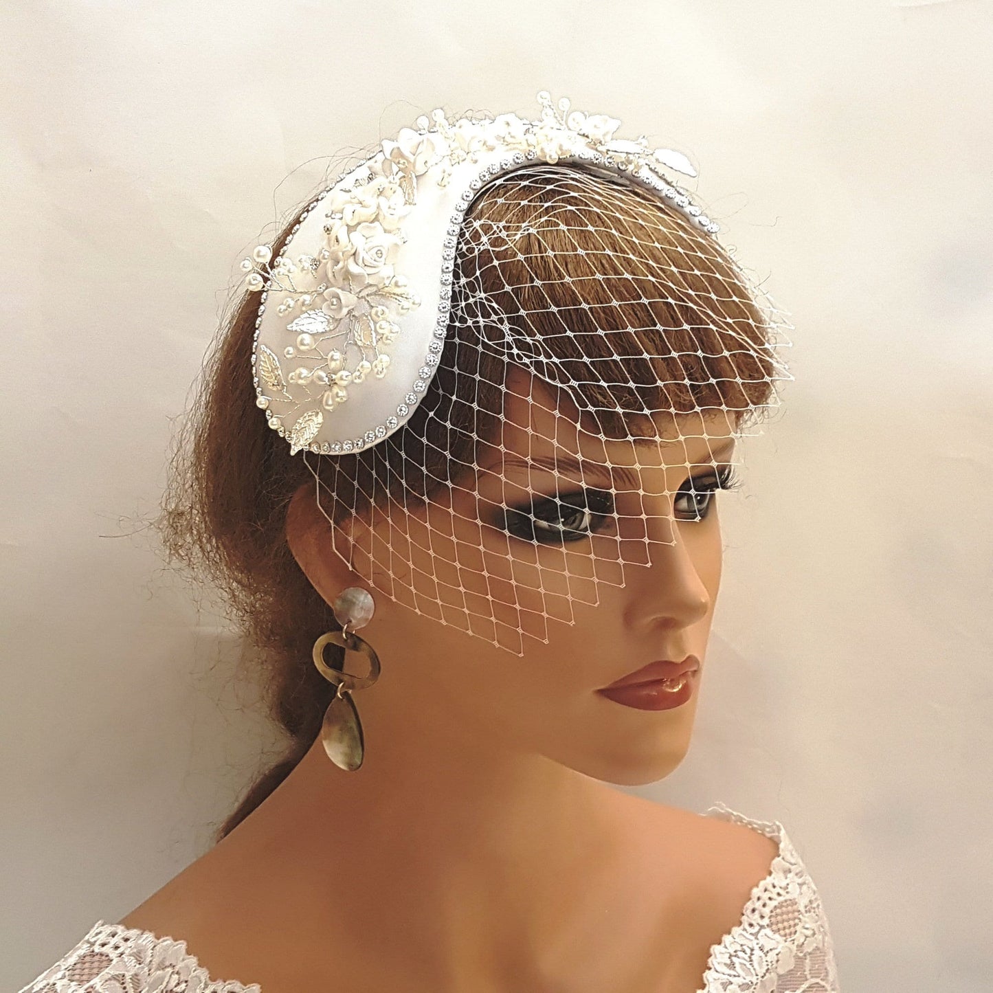 A white satin bridal hat with a pearl and floral embellishment and a white birdcage veil.
