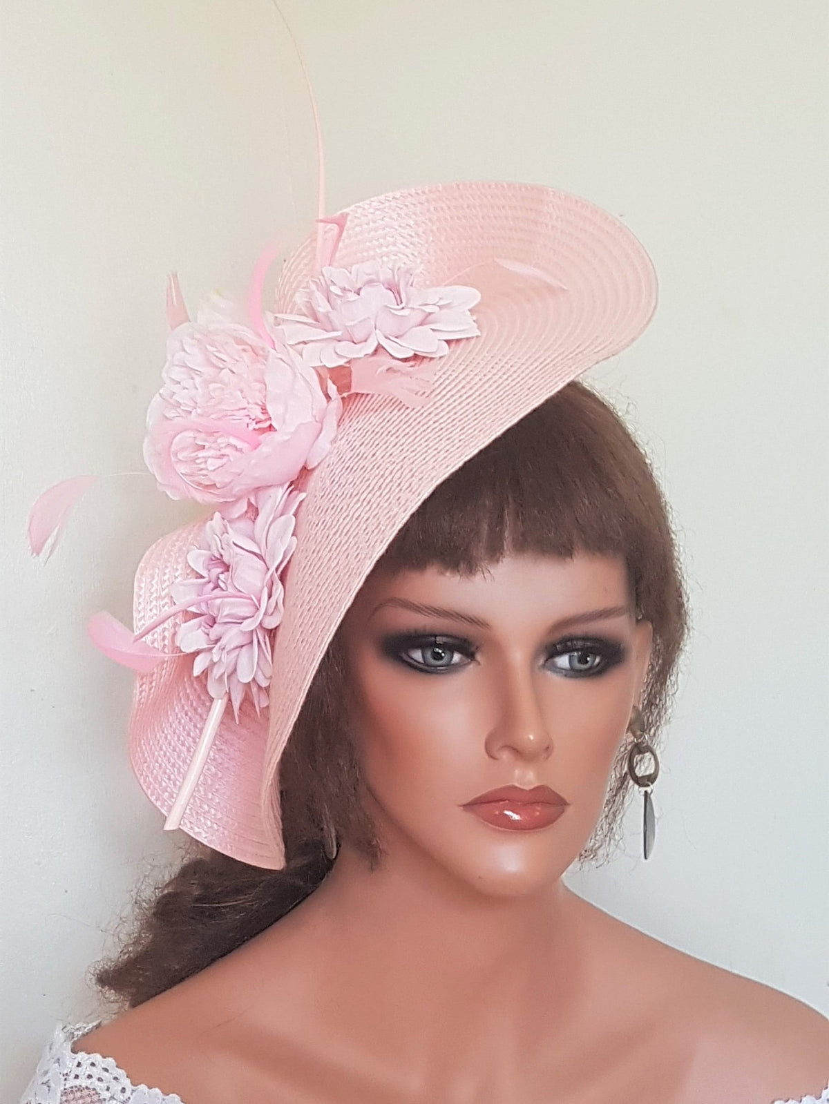 A pink straw hat with a large pink flower and feathers.