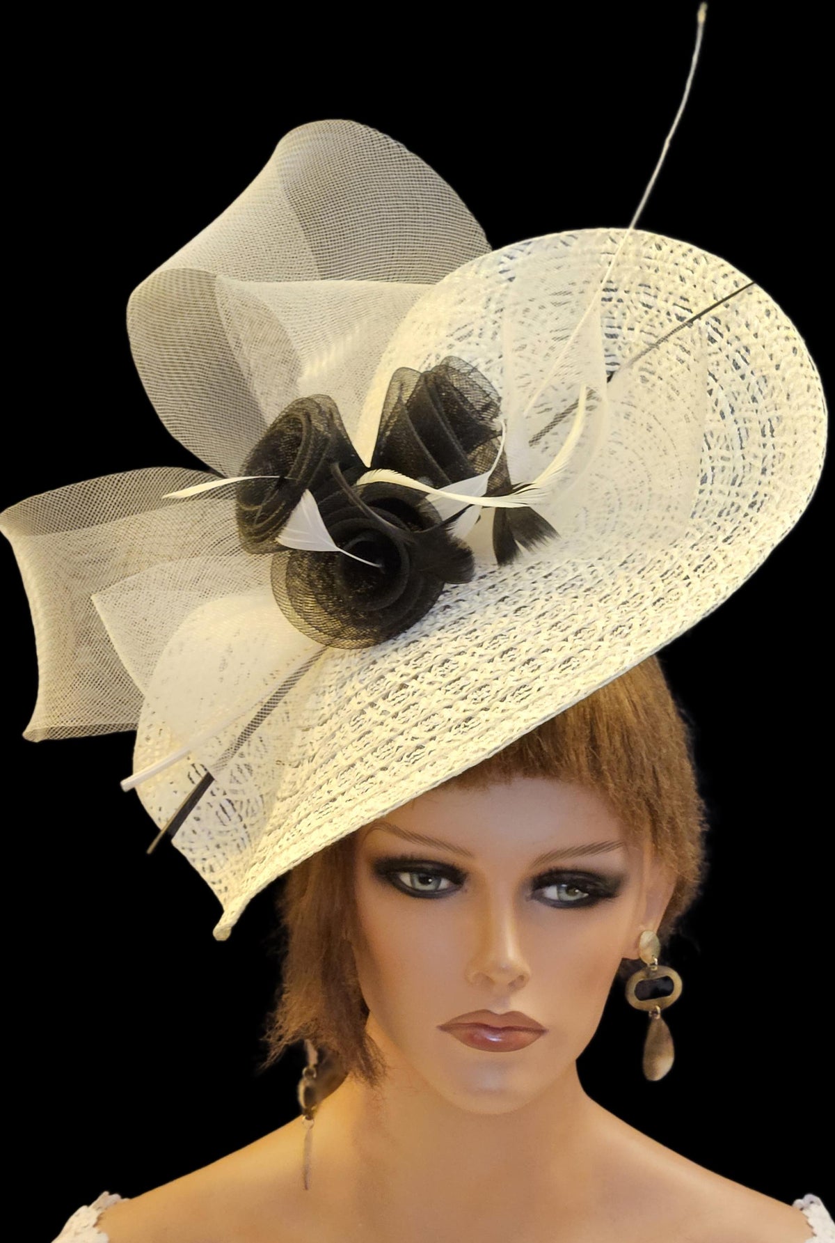 Ivory and black wide-brimmed hat with a large bow and feather embellishments.