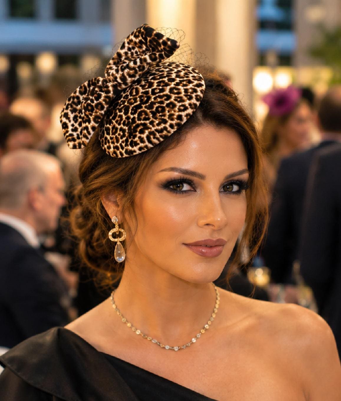May include: A fascinator hat featuring a leopard print pattern with a large bow and a fine black netting veil. The headpiece is worn on the side of the head, showcasing a structured circular base with a soft texture and a classic animal print design.