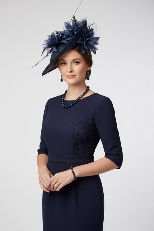 May include: A navy blue dress featuring three-quarter sleeves, a fitted waist, and lace side panels. The ensemble includes a matching navy blue fascinator hat adorned with floral accents, a dark blue beaded necklace, a matching bracelet, and drop earrings.